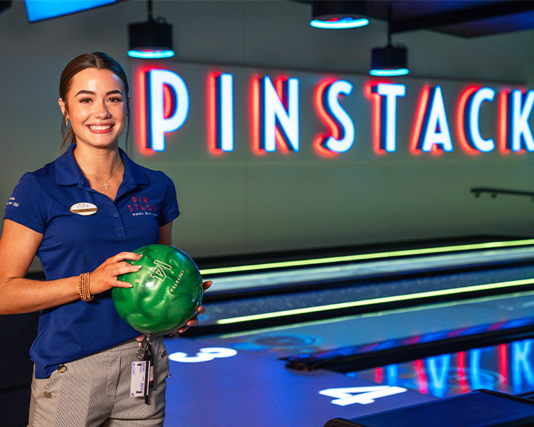 Photo of a smiling manager holding a bowling ball on the lanes.