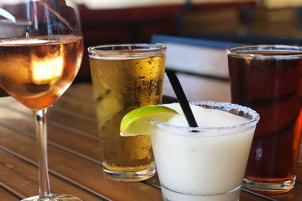 Selection of drinks including rosé, beer, and a frozen margarita with a lime wedge on a patio table during happy hour at PINSTACK.