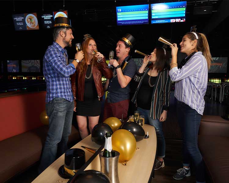 A group of friends blowing horns and toasting to New Year's Eve on the lanes at Pinstack.
